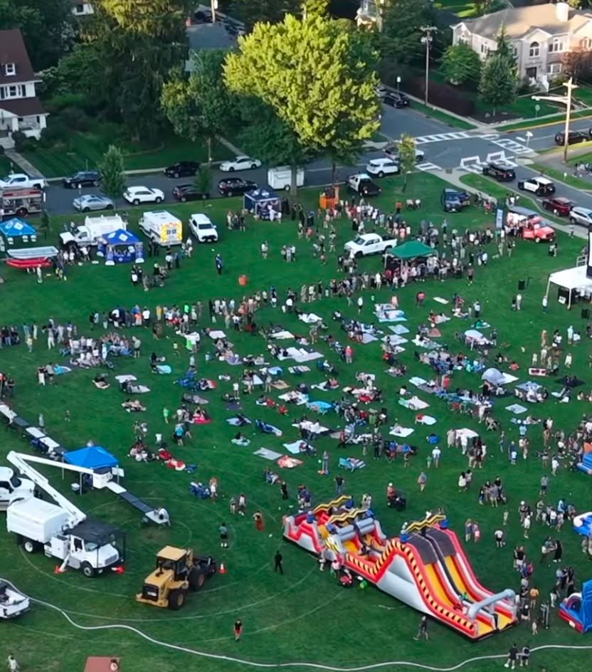 Aerial view of a large outdoor event with a crowd, tents, and an inflatable on a grass field